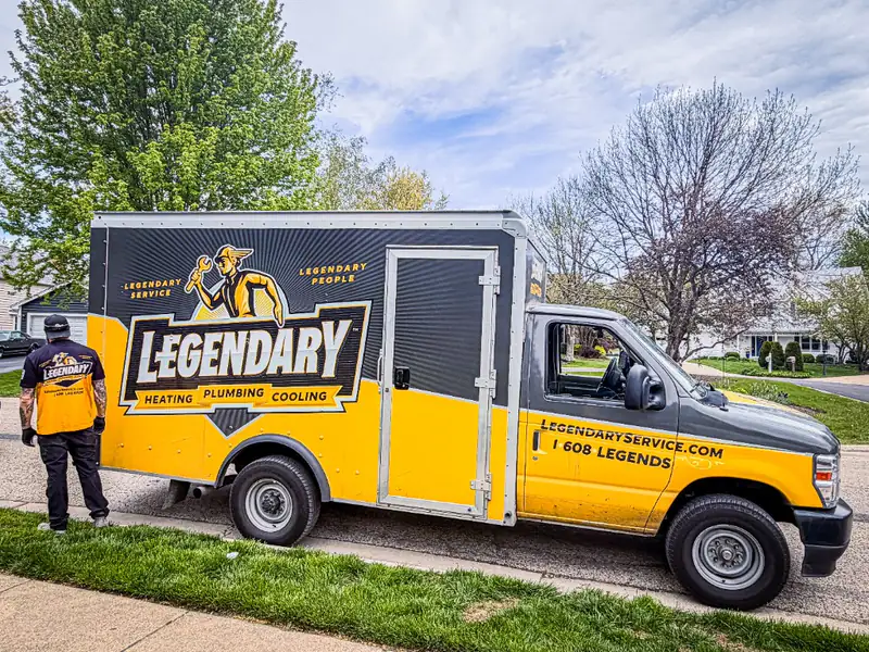 Legendary Service technician in uniform beside a black and gold branded box truck on a residential street