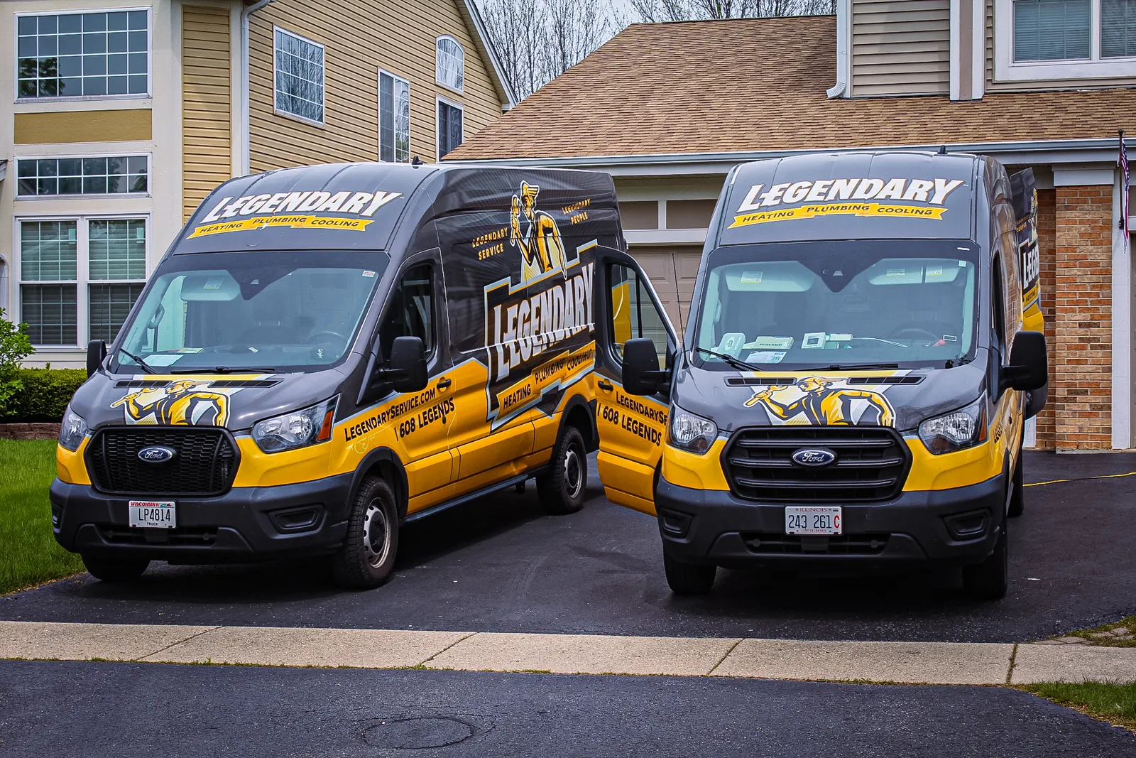 Two Legendary Service branded black and gold vans parked in a driveway
